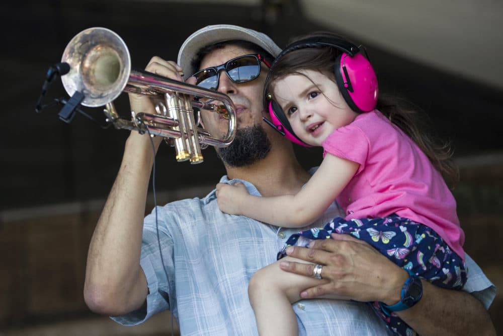 Eric Lucero holds his daughter Ava Lucero, 2, as he plays the trumpet onstage with Sunpie & the Louisiana Sunspots at the Fais Do Do stage during the New Orleans Jazz & Heritage Festival, Sunday, April 28, 2019, in New Orleans. (Alex Brandon/AP)