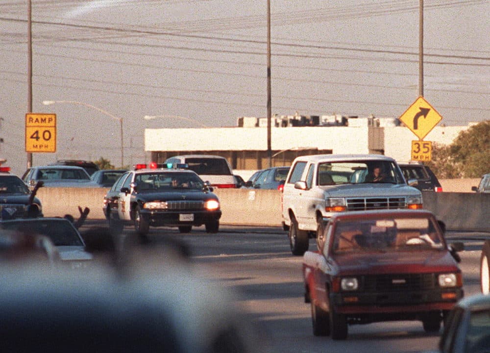 Motorists wave as police cars pursue the Ford Bronco (white, right) driven by Al Cowlings, carrying fugitive murder suspect O.J. Simpson, on a 90-minute slow-speed car chase June 17, 1994 on the 405 freeway in Los Angeles, Calif. (Mike Nelson/AFP/Getty Images)