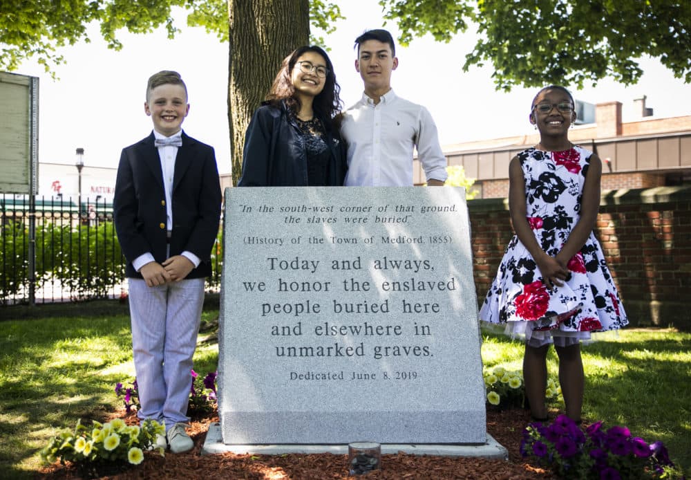 Medford Public Schools students Liam Brady, Jenny Lu, Joseph Schmidt and Jasmine Hagbourne stand for a photo at the unveiling ceremony of the Medford Slavery Memorial in Salem Street Burying Ground. The students organized the creation of a memorial to a group of more than 50 slaves who were buried in unmarked graves in the Salem Street Cemetery.  (Erin Clark for WBUR)