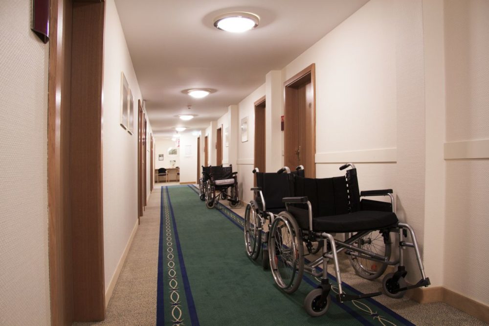 A few empty wheelchairs sit against the wall of an hallway.