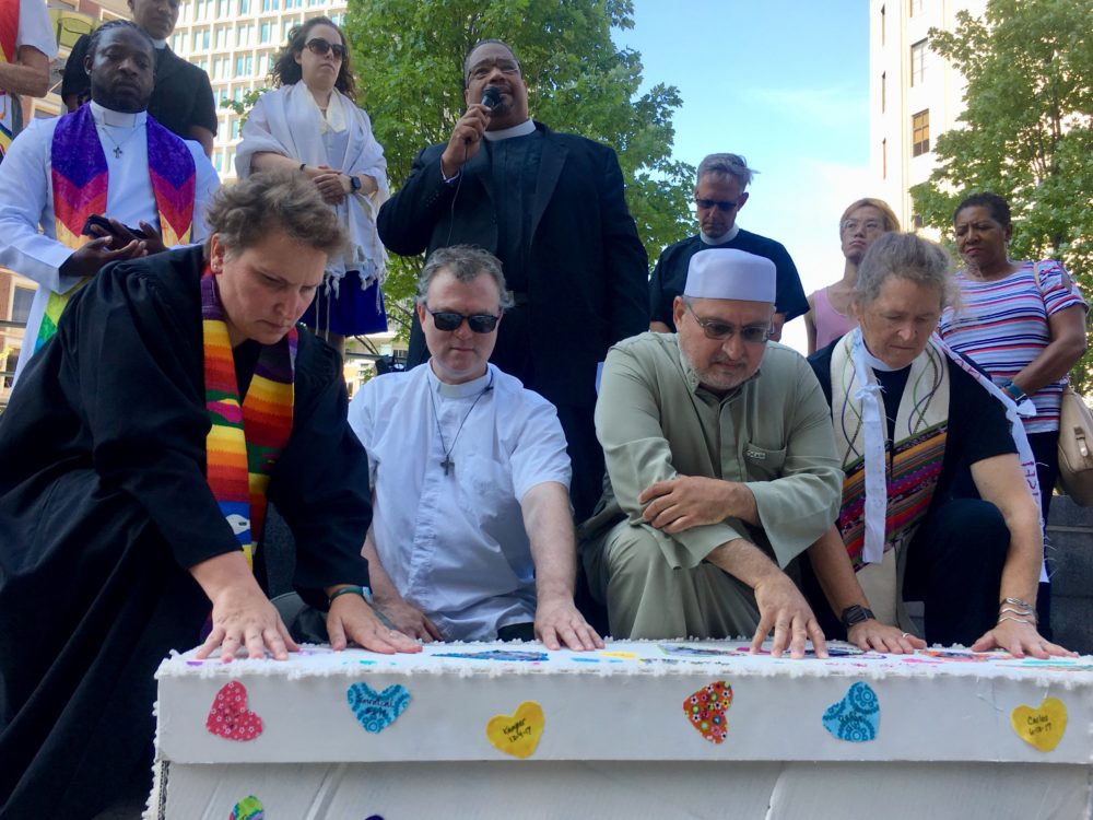 Clergy members knelt over a coffin bearing the names and photos of migrant children who died in U.S. custody Monday to kick off a six-day march protesting immigrant detention and deportation. (Katie Lannan/SHNS)