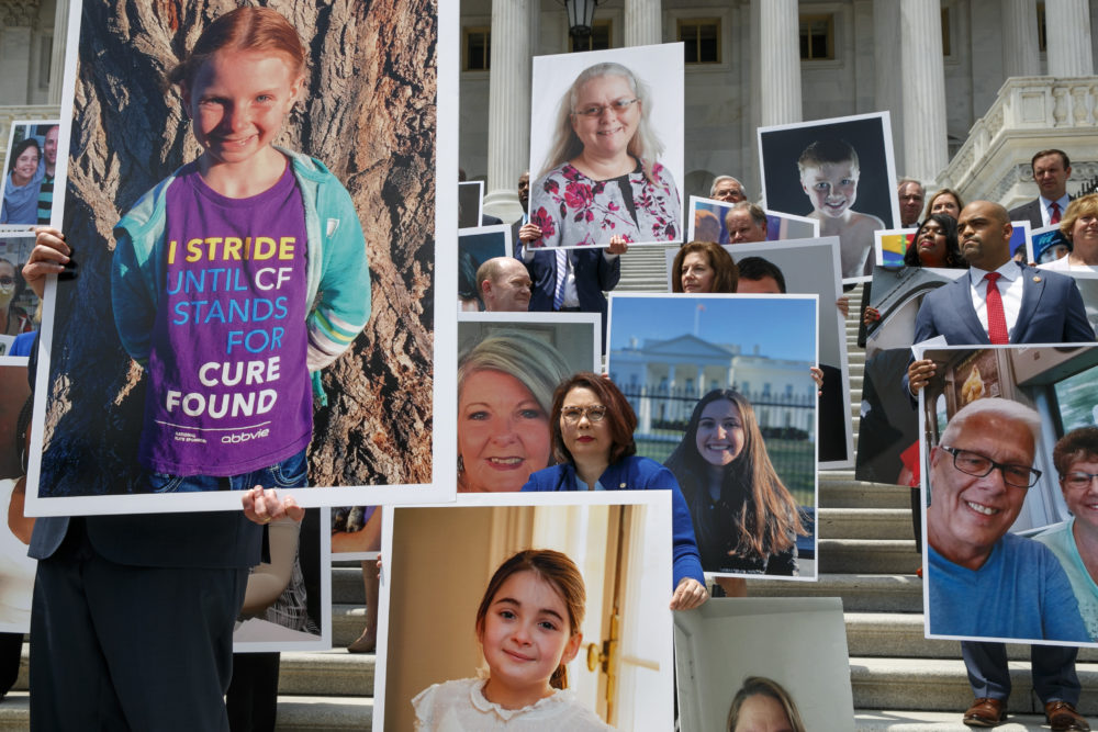 Sen. Tammy Duckworth, D-Ill., center, attends a news conference on health care among photos of people with preexisting conditions at the Capitol on July 9 in Washington. At right is Rep. Colin Allred, R-Texas. (Jacquelyn Martin/AP)