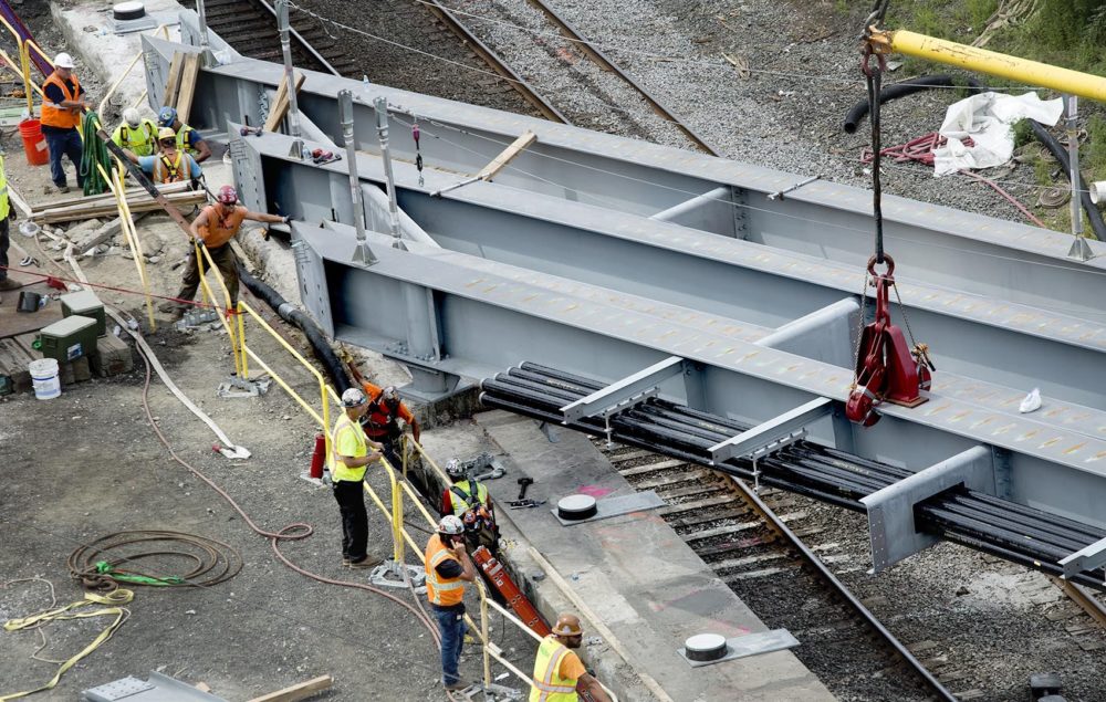 Construction workers ease a new steel beam into position as part of work to replace the the Commonwealth Avenue Bridge in July 2018. (Robin Lubbock/WBUR)