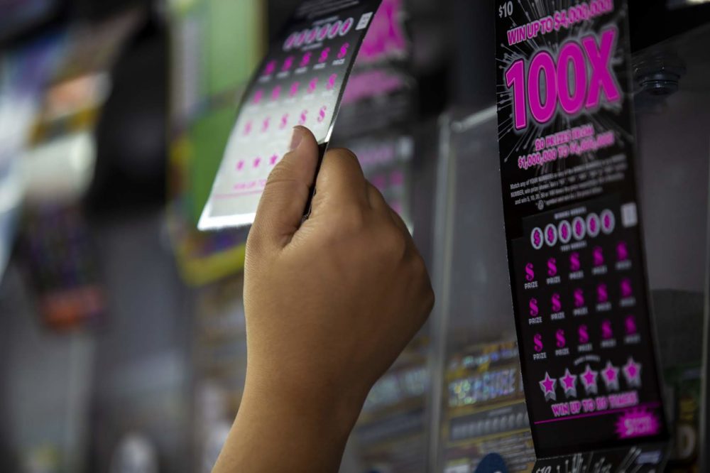 A cashier at College Convenience on Huntington Avenue pulls a scratch ticket from the lottery ticket display to sell to customer. (Jesse Costa/WBUR)