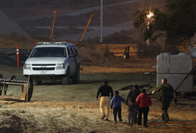 In this Dec. 3, 2018 file photo, migrants are escorted by a U.S. Border Patrol agent as they are detained after climbing over the border wall from Playas de Tijuana, Mexico, to San Ysidro, Calif.  (Rebecca Blackwell/AP)