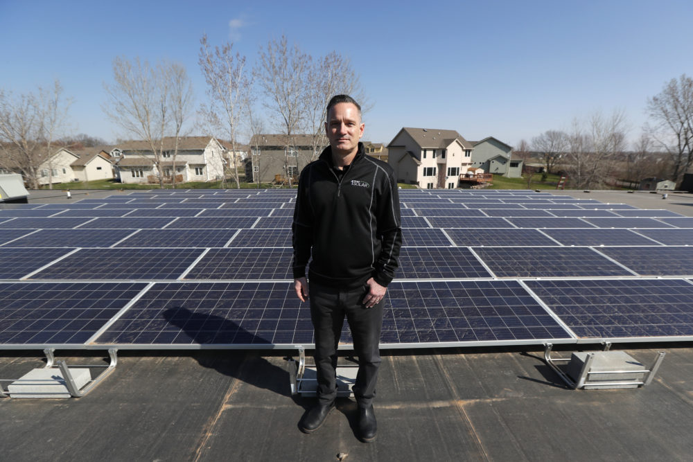 Todd Miller stands next to solar panels on the roof of his solar installation business in Ankeny, Iowa. For years wind and solar were friendly twins in the campaign for green alternatives to fossil fuels, but the relationship is getting ugly in a number of states, especially in Iowa, where more than 4,000 turbines generate 37% of the state’s electricity, the second highest rate in the country. (Charlie Neibergall/AP)
