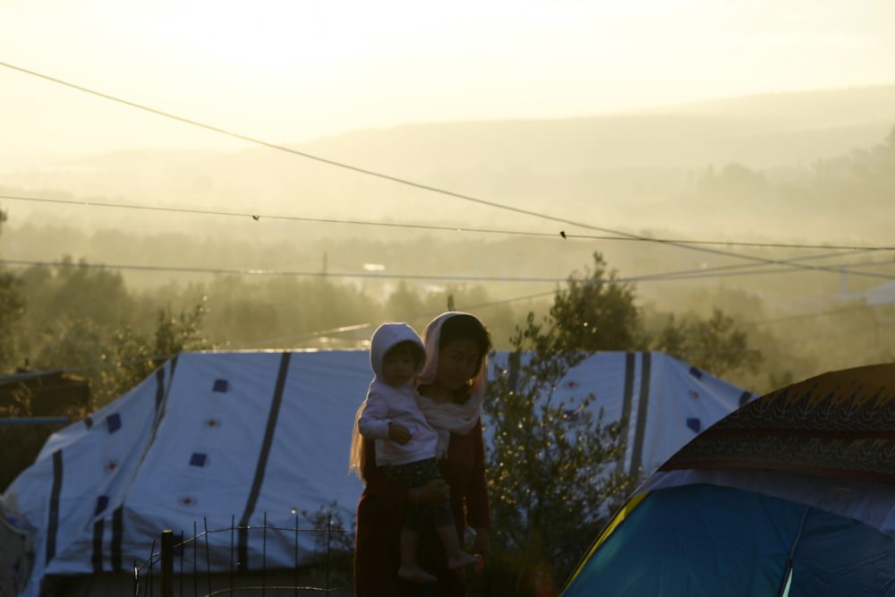 A woman holds a baby as the sun rises outside the Moria refugee camp on the northeastern Aegean island of Lesbos, Greece, Wednesday, Sept. 25, 2019. Authorities on the Greek island of Lesbos have partly reopened the country's largest refugee camp to newly arrived migrants despite acute overcrowding. (Michael Varaklas/AP)