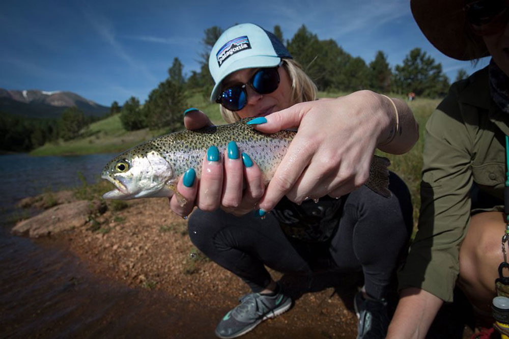 Lauren McKenzie of Colorado Springs lands her very first trout, caught on a dry fly. Flyfishing guide Kaitlin Boyer introduced McKenzie to the sport in July at South Catamount Reservoir behind Pikes Peak. (Photo by Hart Van Denburg/CPR News)