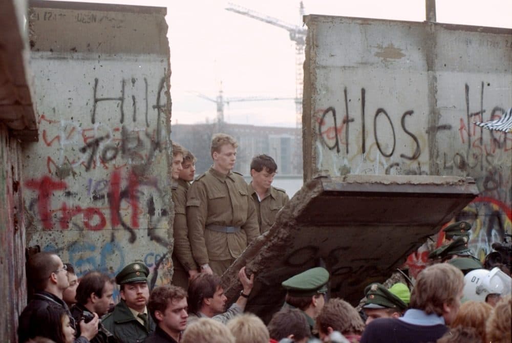 This Nov. 11, 1989 photo shows East German border guards looking through a hole in the Berlin wall after demonstrators pulled down one segment of the wall at Brandenburg gate. (Lionel Cironneau/File/AP)