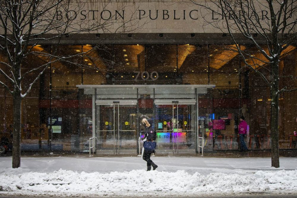 A woman walks by the Boston Public Library during the morning snowfall. (Jesse Costa/WBUR)