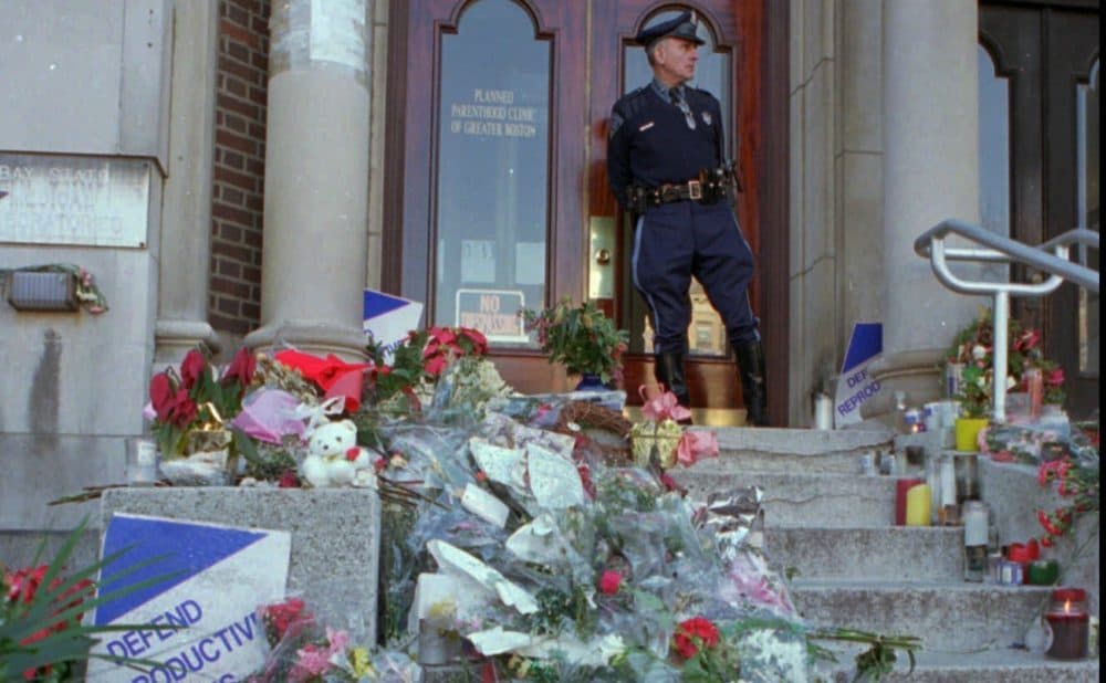 In this Wednesday, Jan. 4, 1995 file photo, Masssachusetts State Trooper Daniel Dhionis stands guard at the Planned Parenthood Clinic of Greater Boston in Brookline, Mass,, where flowers and letters were left after two women were killed, and five people injured in shootings at Planned Parenthood and another clinic. Planned Parenthood clinics have been repeated targets of bombings, arson and protests. (Julia Malakie/AP)