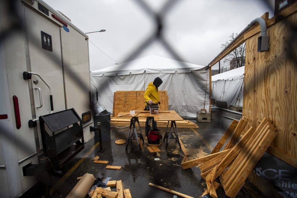 A contractor picks up a box of screws from a work bench during construction of tents for people who are homeless and affected by the coronavirus behind the Southampton Street shelter in Boston. (Jesse Costa/WBUR)