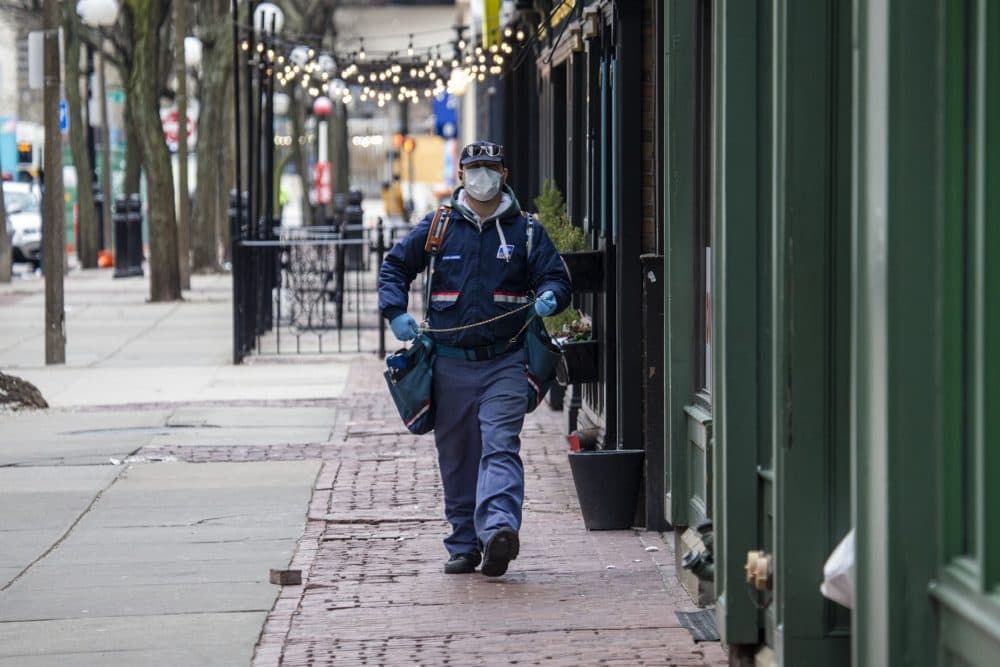 A U.S. postal mail carrier with a mask delivers mail on Canal Street by North Station. (Jesse Costa/WBUR)