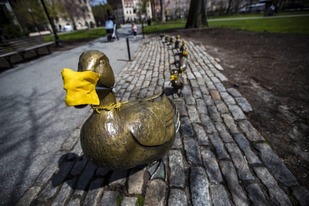 In this photo from April 10, all of the ducks of the &quot;Make Way for Ducklings&quot; sculpture in the Boston Public Garden don yellow masks. (Jesse Costa/WBUR)