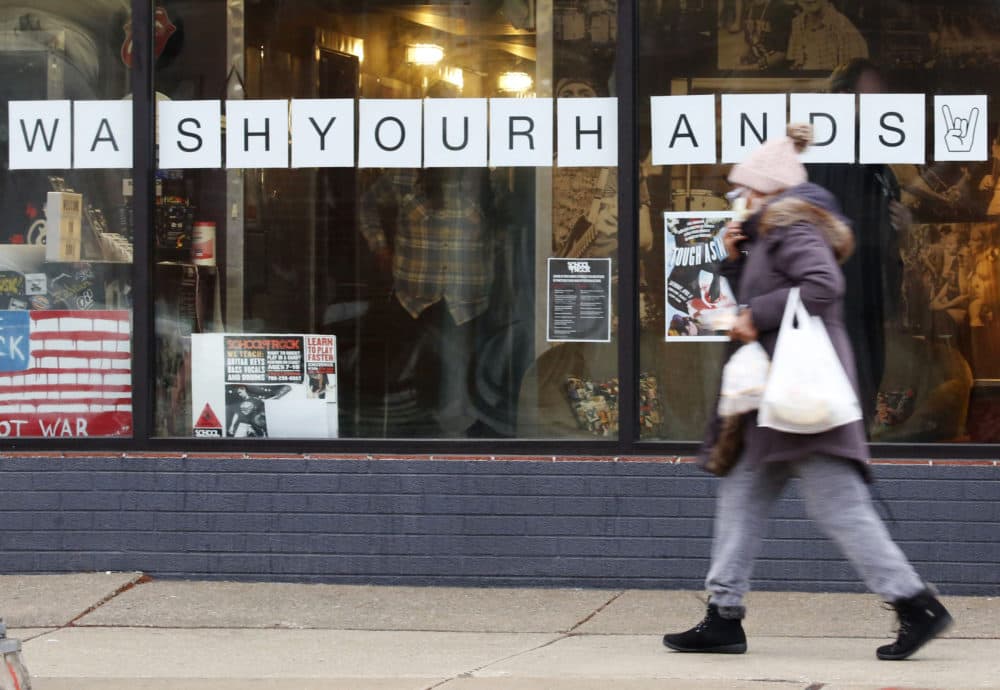 In this March 19, 2020, photo, a woman in a face mask walks past a &quot;Wash Your Hands&quot; sign after buying groceries in Oak Park, Ill., before a two-week &quot;shelter in place&quot; order goes into effect. (Martha Irvine/AP)