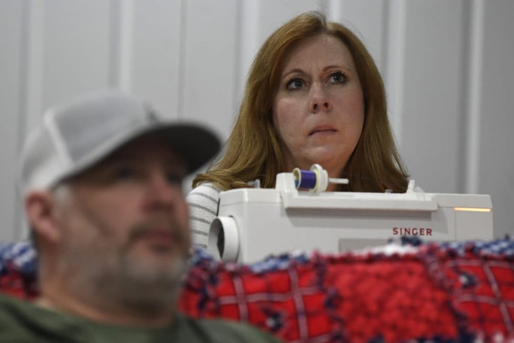 Jennifer Snead sitting in front of her sewing machine, and her husband Buddy Snead, both of Annapolis, Md., take a pause as they watch a news conference with Maryland Gov. Larry Hogan in their Annapolis home, Monday, March 23, 2020. (Susan Walsh/AP)