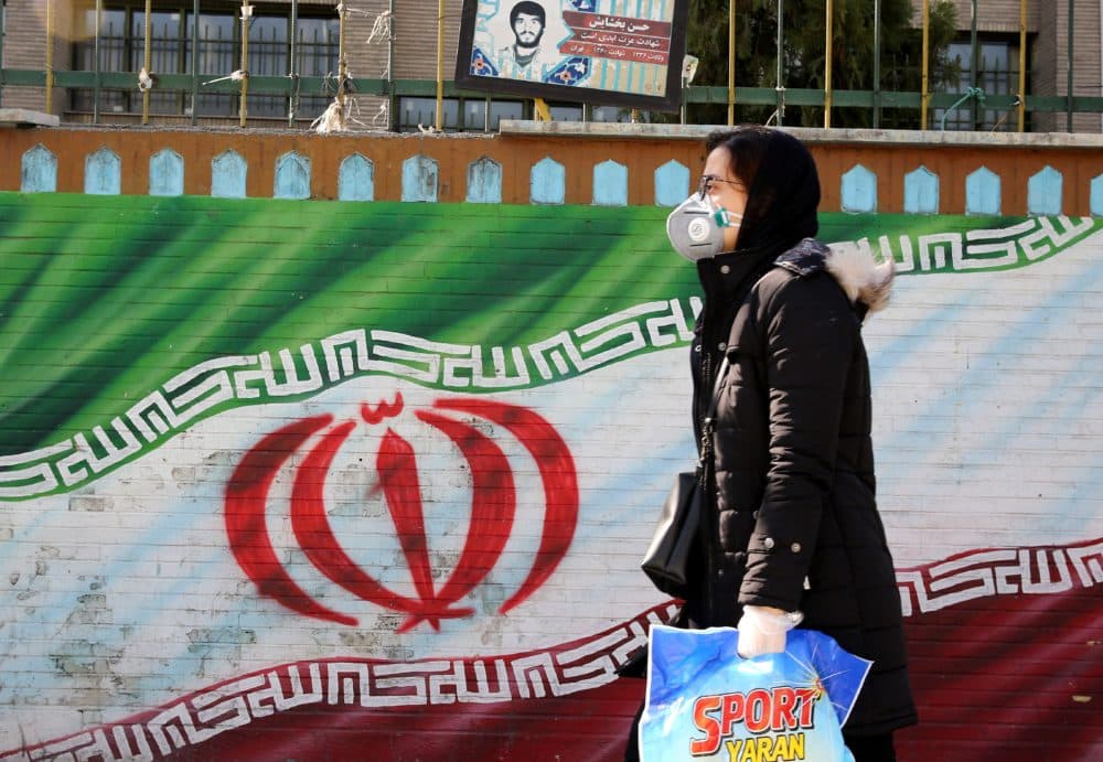 An Iranian woman wearing a mask walks past a mural displaying her national flag in Tehran. (Atta Kenare/AFP via Getty Images)