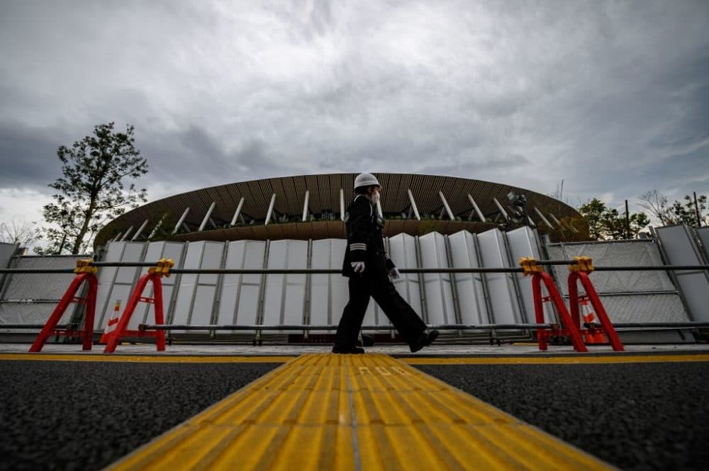 A security guard wearing a face mask walks in front of a construction site at the Japan National Stadium in Tokyo three days after the historic decision to postpone the 2020 Tokyo Olympic Games. (Philip Fong/AFP via Getty Images)
