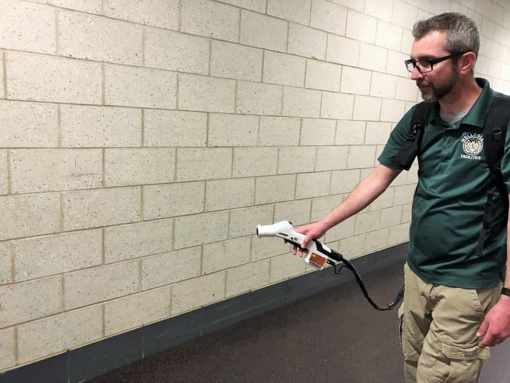 Tony Vassiliadis, the head nighttime custodian at Wellesley High School, demonstrates an electrostatic sprayer. During real usage, he would wear gloves and an N95 mask. (Callum Borchers/WBUR)