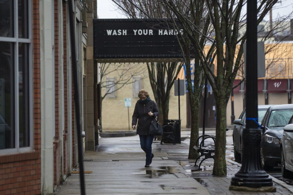 A woman walks past a closed Norwood Cinema where the marquee reads &quot;Wash your hands.&quot; (Jesse Costa/WBUR)