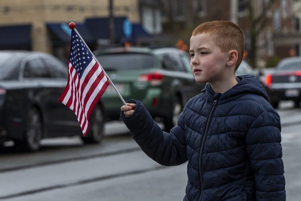 A young boy pays his respects to Mary Foley, waving a flag as her funeral procession passes. (Jesse Costa/WBUR)
