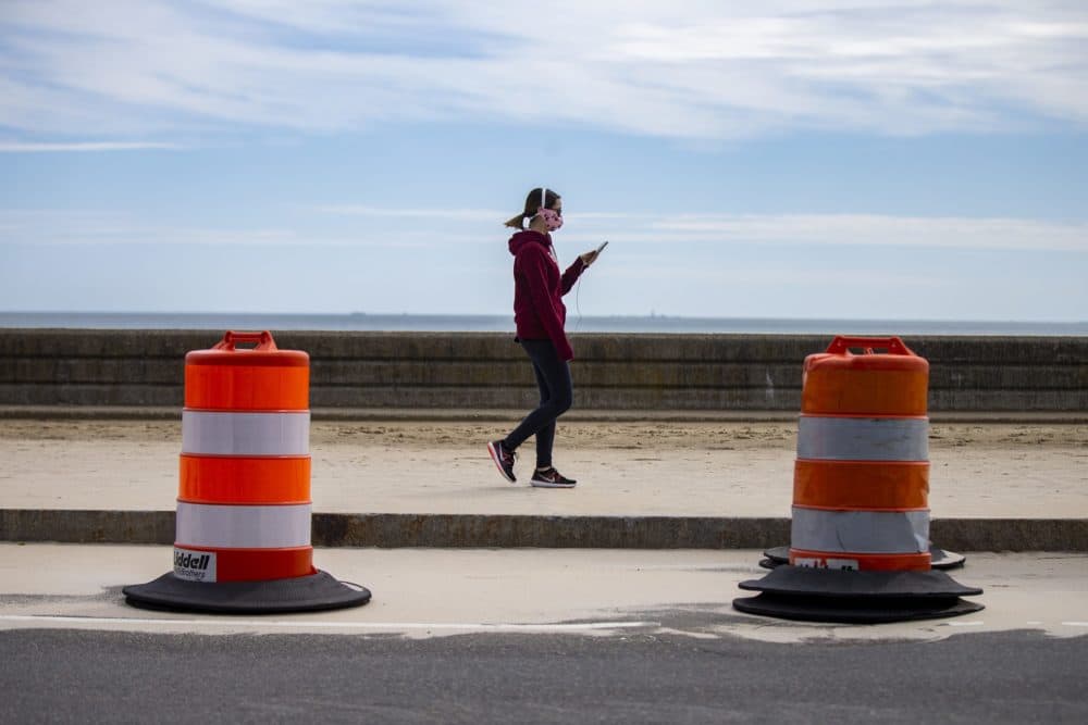 A woman looks at her phone while walking along Revere Beach. (Jesse Costa/WBUR)
