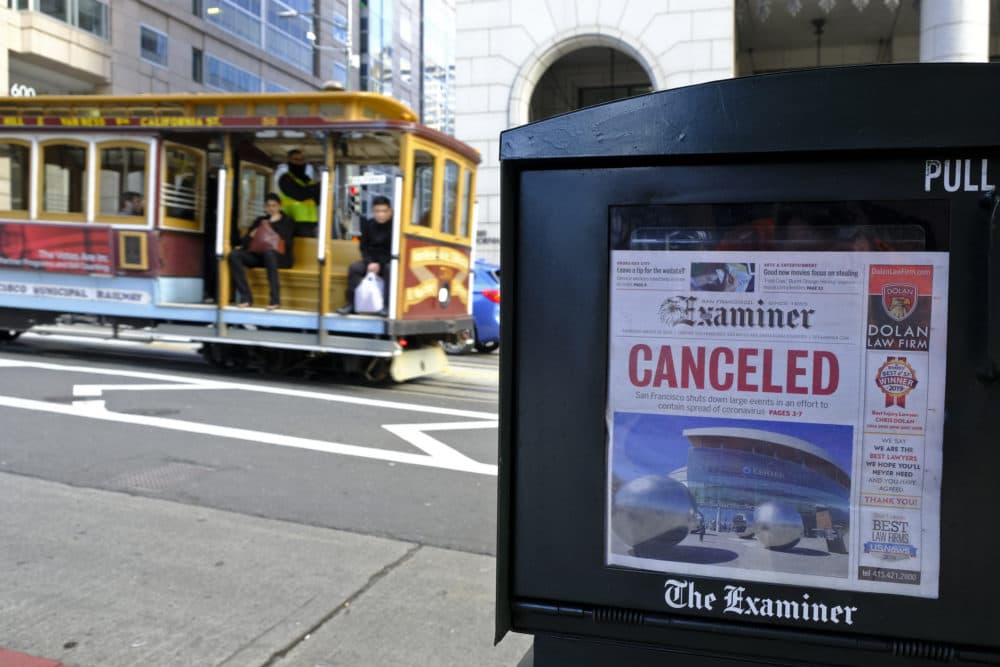 A newspaper headline announcing the closure of large events is displayed as a cable car goes down California Street, Friday, March 13, 2020, in San Francisco. (Eric Risberg/AP Photo)