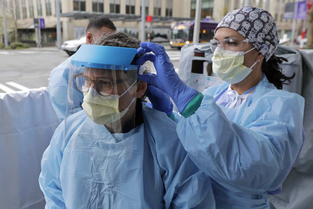 In this April 2, 2020 photo, Tilliesa Banks, right, an emergency services nurse at Harborview Medical Center in Seattle, helps a colleague put on a medical face shield. (Ted S. Warren/AP)