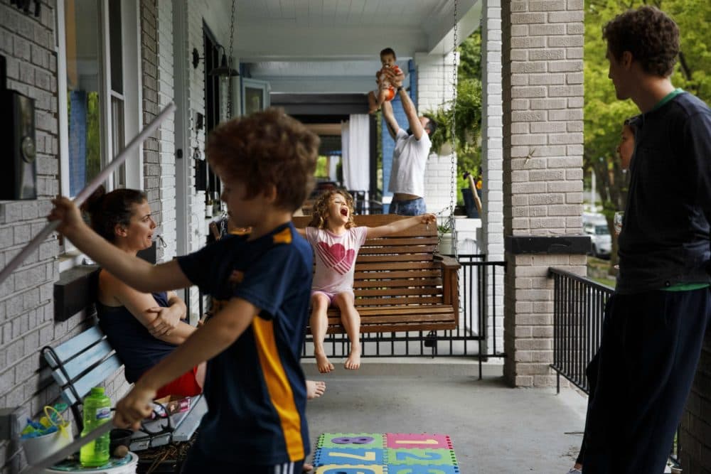 Carys Williams, 7, center, plays on the family porch swing as her brother Owain, 8, left, plays with metal rods, and Gavin Tropeano, 9 months, is swung up in the air by his father Andrew Tropeano, as neighbors spend extra time on their porches since schools and offices closed due to the coronavirus, Sunday April 5, 2020, in Washington. (Jacquelyn Martin/AP)