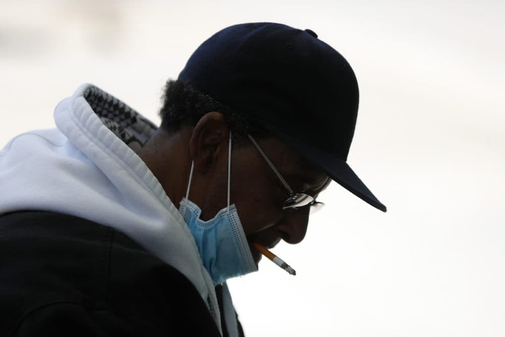 A man smokes a cigarette while wearing a protective mask while waiting for a bus in Detroit. (Paul Sancya/AP)