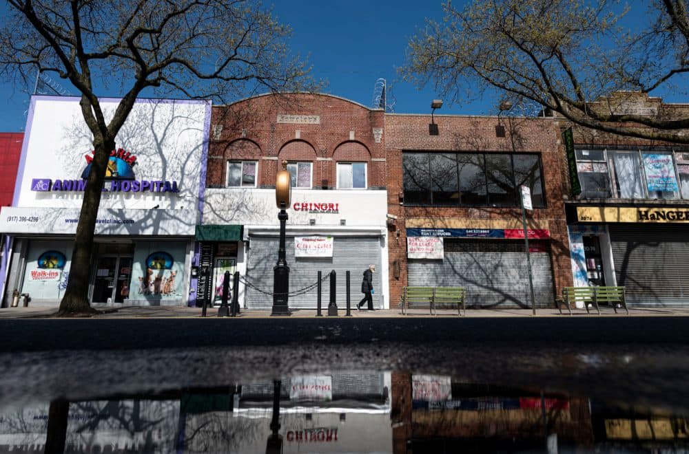 A woman wearing a mask walks past closed store fronts in the Astoria neighborhood of Queens, on April 15, 2020 in New York City. (JOHANNES EISELE/AFP via Getty Images)
