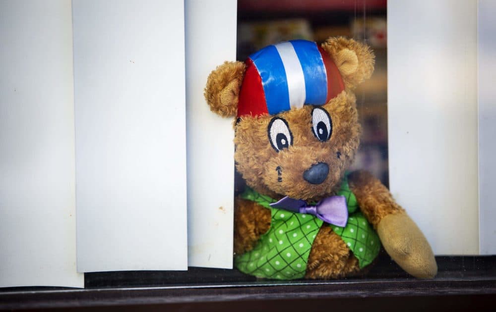 A stuffed toy looks out through the shades of a window onto the street at Play Academy in Medford, perhaps wondering when his friends will return. (Robin Lubbock/WBUR)