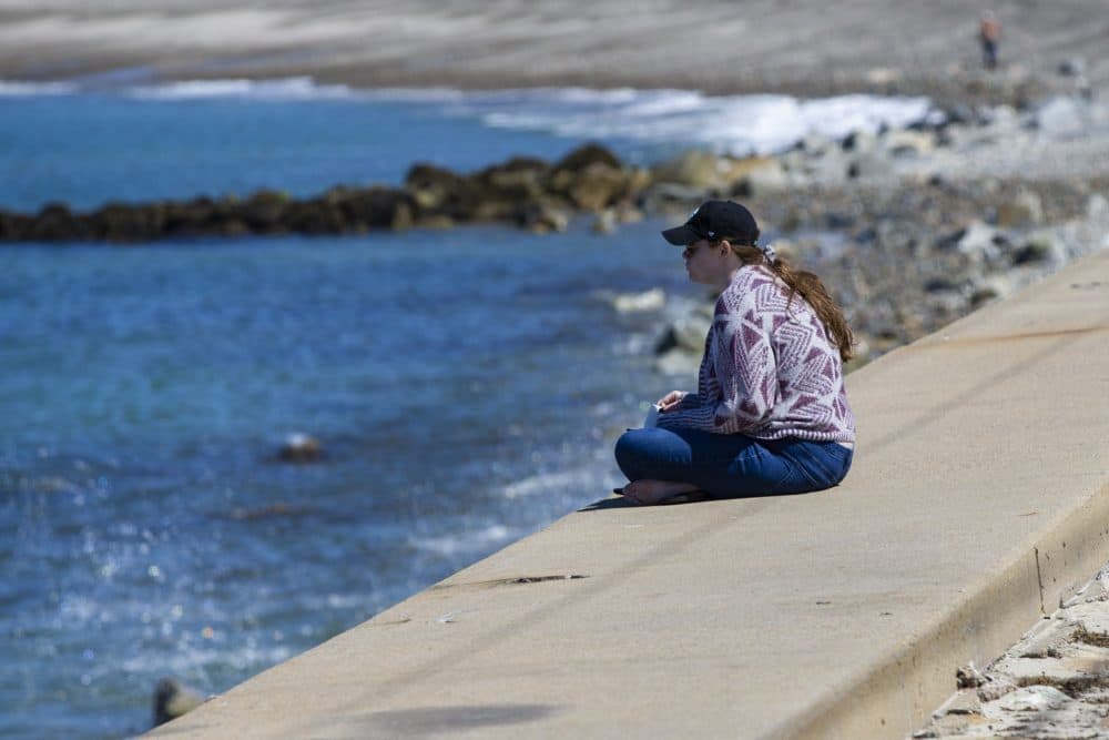 A woman sits alone on the seawall of Brant Rock Beach. (Jesse Costa/WBUR)