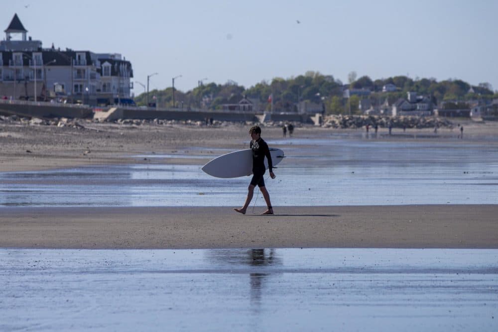 A surfer walks back to the beach on Nantasket Beach in Hull. (Jesse Costa/WBUR)