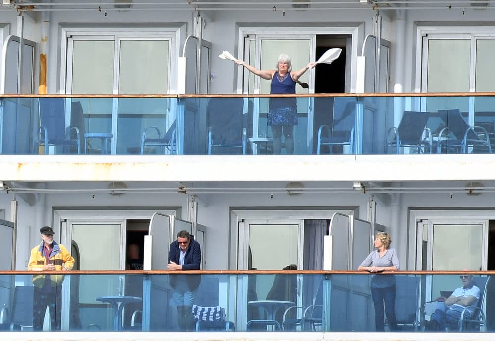 A woman gestures as other people look on from aboard the Grand Princess cruise ship, operated by Princess Cruises, as it maintains a holding pattern about 25 miles off the coast of San Francisco, California on March 8, 2020. (JOSH EDELSON/AFP via Getty Images)