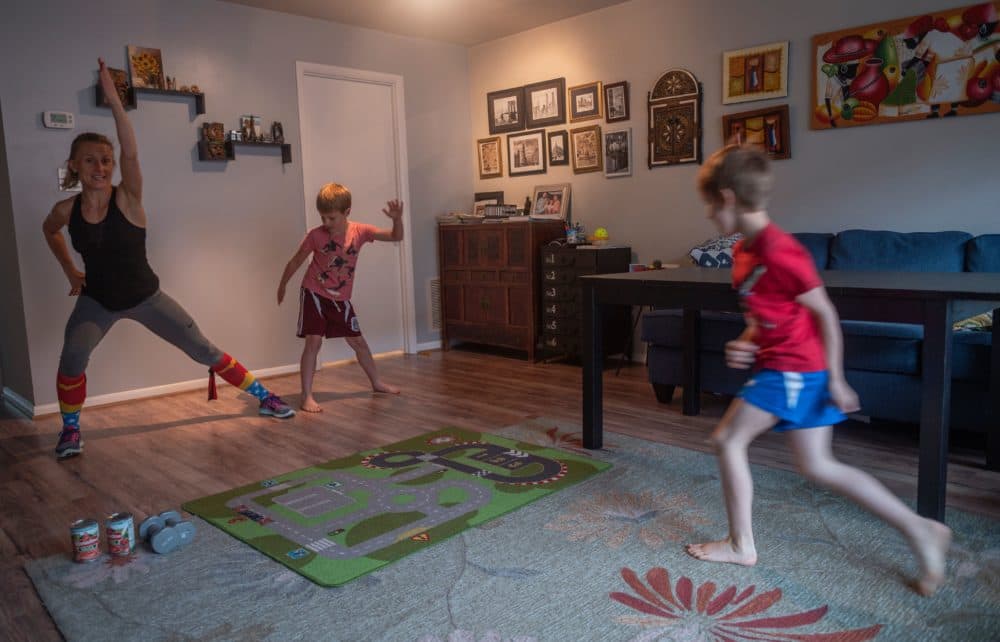 Mimicked by her son Daniel (C), Paulina Mansz, a group fitness instructor, records a workout session for her clients while her other son Javier plays, as she continues to instruct from home in Arlington, Virginia on April 30, 2020. (Photo by ANDREW CABALLERO-REYNOLDS/AFP via Getty Images)