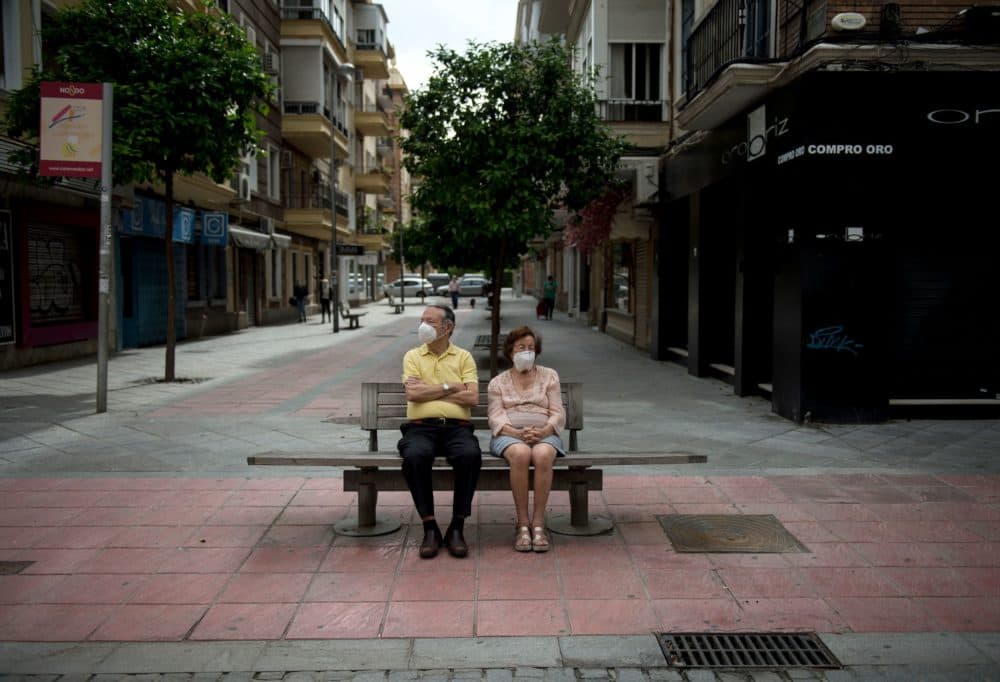 A couple wearing face masks sits on a bench in Seville, Spain, on May 7, 2020, as the country prepares to ease its tough lockdown measures. (Cristina Quicler/AFP/Getty Images)