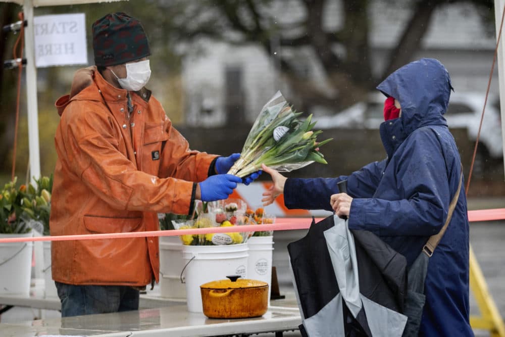 David Baecher sells flowers to a customer at a farmer's market, Friday, May 1, 2020, in Brunswick, Maine. Gov. Janet Mills is requiring that people wear masks in public to help prevent the spread of the coronavirus as part of her business reopening plan. (AP Photo/Robert F. Bukaty)