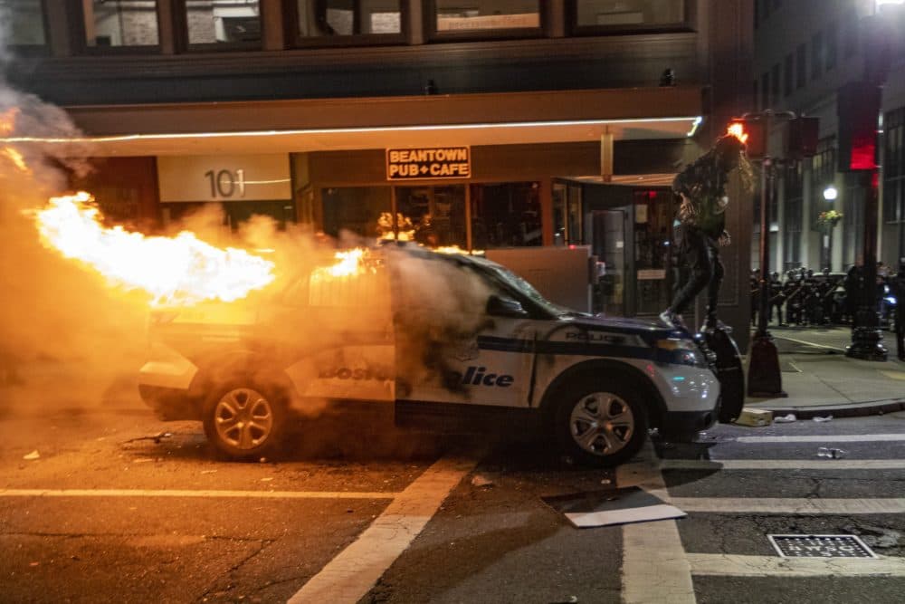 A protester walks on a Boston Police cruiser set fire on Tremont Street after a March 31 protest near the Massachusetts 
State House. (Jesse Costa/WBUR)