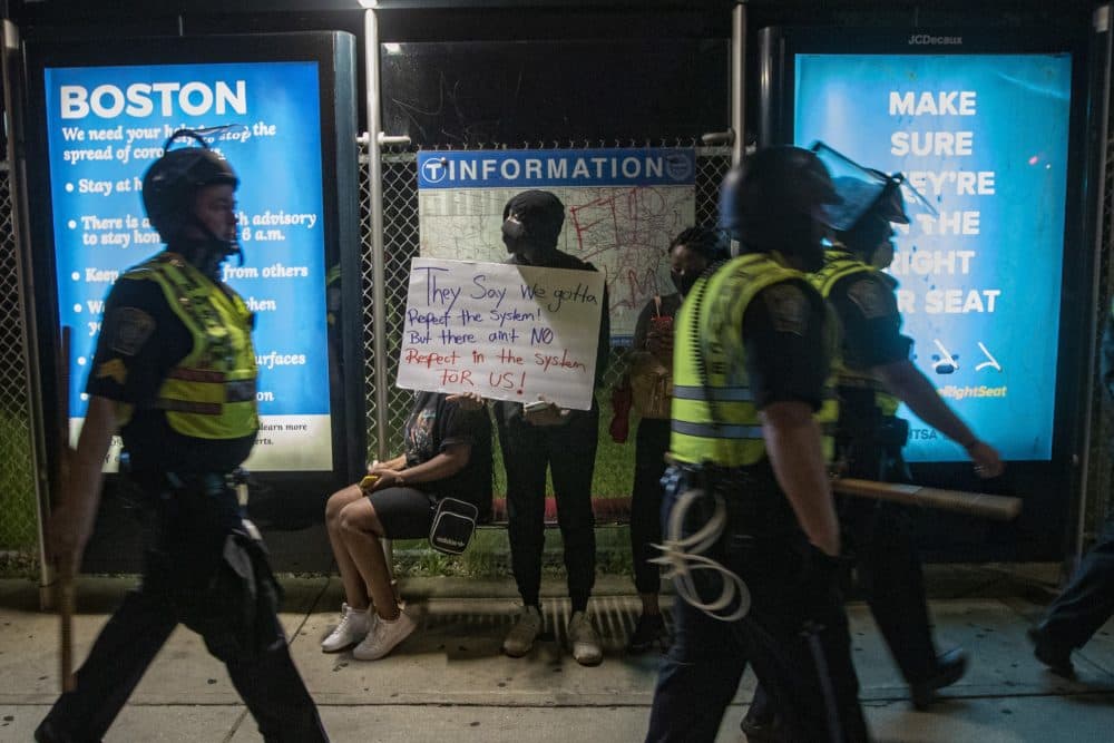 Boston Police walk past protesters waiting in a bus stop on Washington Street in Jamaica Plain. (Jesse Costa/WBUR)