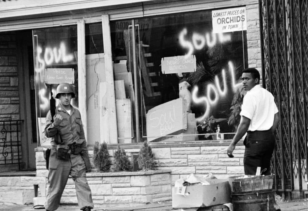 In this July 15, 1967 file photo a National Guard officer passes the smashed window of a Black-owned flower shop in riot-torn Newark, N.J. The last surviving member of the Kerner Commission says he remains haunted that the panel's recommendations on U.S. race relation and poverty were never adopted, but he is hopeful they will be one day. (AP Photo,File)