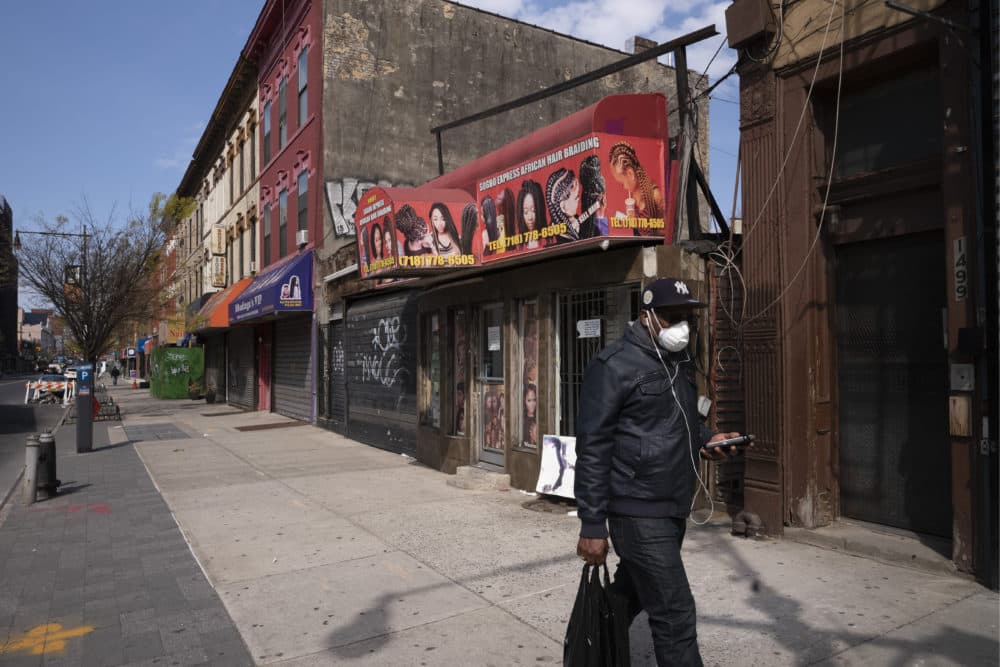 A man wearing a mask walks past Sogho Express African Hair Braiding salon, which is closed due to the coronavirus pandemic, Tuesday, April 7, 2020 in the Bedford Stuyvesant neighborhood of New York. (Mark Lennihan/AP)