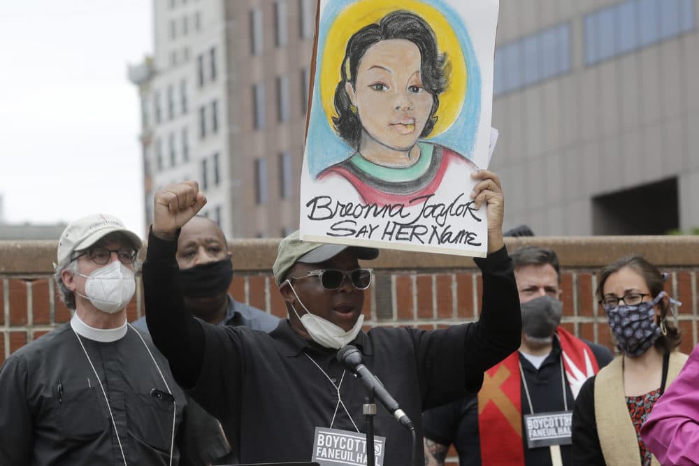 Kevin Peterson, founder and executive director of The New Democracy Coalition, center, displays a placard showing fallen Breonna Taylor as he addresses a rally n Boston. Petersen advocates for changing the name of Faneuil Hall, as its namesake Peter Faneuil, was a slave owner. (Steven Senne/AP)