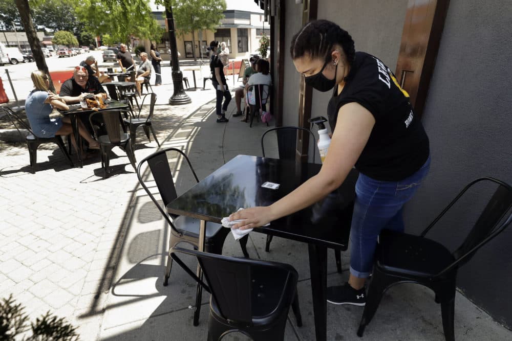 In this June 18, 2020, file photo, Jayda Boykin, of Norwood, Mass., a worker at Lewis' Bar and Grille, cleans a table and chairs, in an outdoor dining area on a sidewalk at the restaurant, in Norwood, Mass. (Steven Senne/AP File Photo)