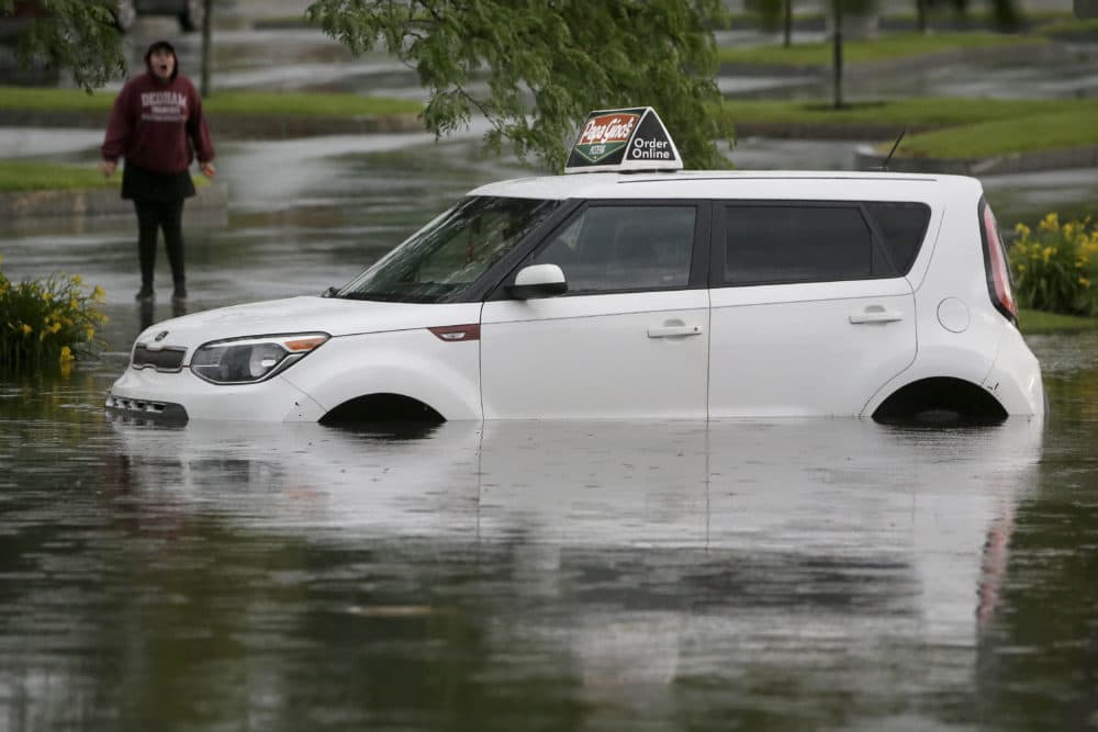 A woman speaks to a person in a vehicle stranded in water on Sunday on a flooded street in Norwood, Mass. (Steven Senne/AP)