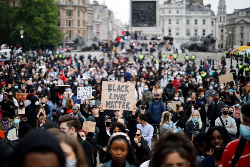 Activists, some wearing face coverings or face masks as a precautionary measure against COVID-19, hold placards as they attend a Black Lives Matter protest in Trafalgar Square in London on June 12, 2020, backdropped by the Houses of Parliament. (Tolga Akmen/AFP via Getty Images)