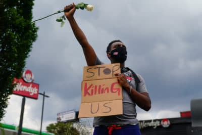 A man holds a sign and a white rose in his fist while facing traffic outside a burned Wendy's restaurant on the second day following the police shooting death of Rayshard Brooks in the restaurant parking lot June 14, 2020, in Atlanta, Georgia. (ELIJAH NOUVELAGE/AFP via Getty Images)