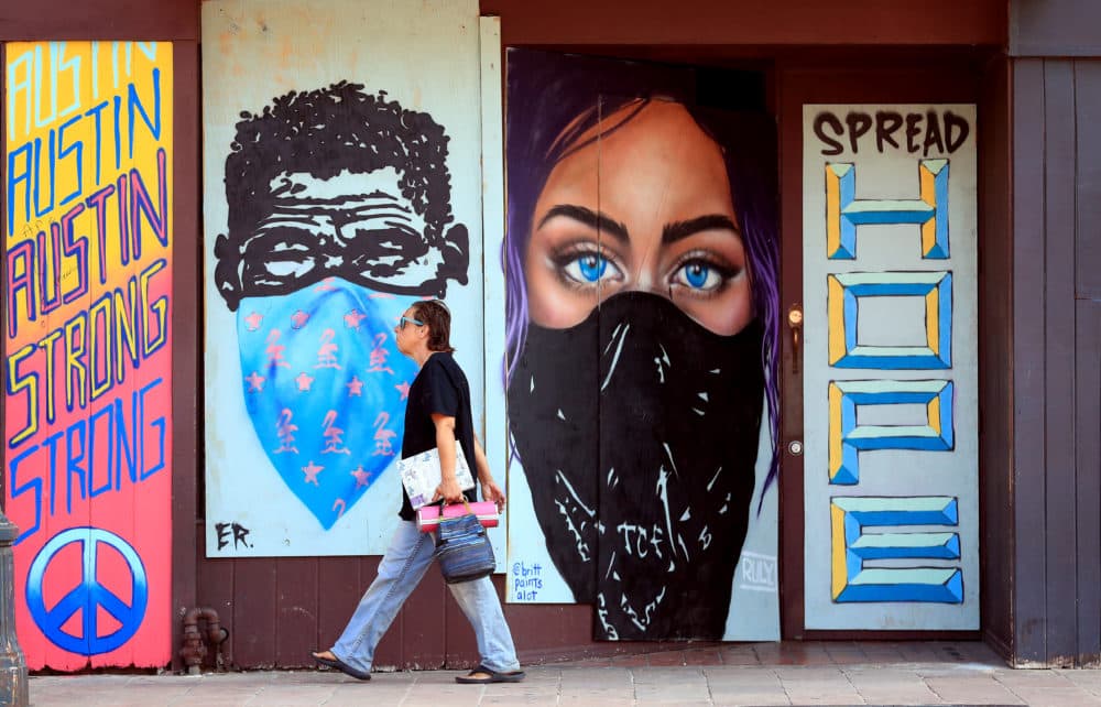 Pedestrians walk past murals painted on boards covering bar windows on 6th Street on May 20, 2020 in Austin, Texas. (Tom Pennington/Getty Images)