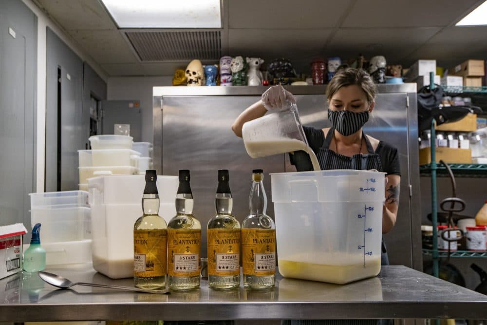 Brit McMahan, manager at Drink in Boston, pours coconut milk into a container of pineapple juice while preparing a batch of piña colada for take out. (Jesse Costa/WBUR)