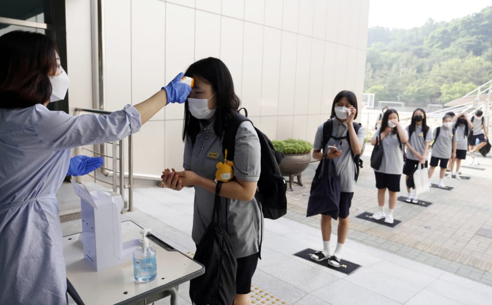 Students wearing face masks to help protect against the spread of the novel coronavirus stand in a line to have their body temperatures checked before entering their classrooms at a middle school in Chungju, South Korea, Monday, June 8, 2020. (In Jin-hyun/Newsis via AP)